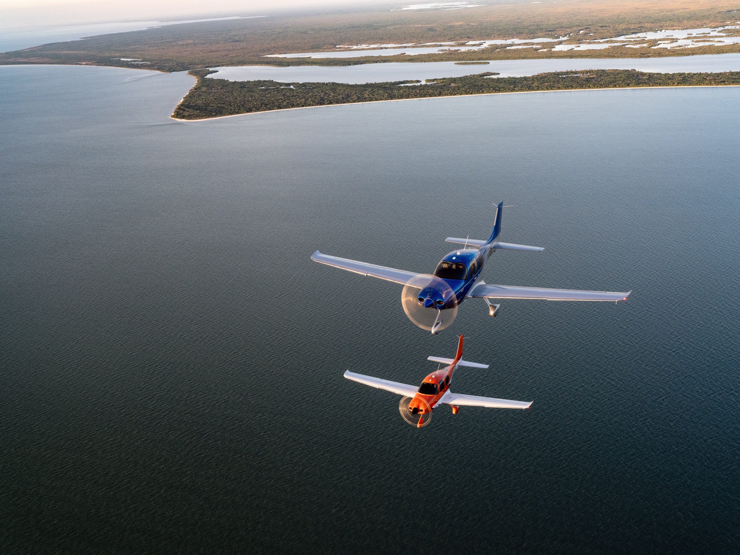 Two Cirrus SR aircraft flying together over the coast